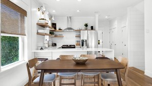 A modern kitchen with white cabinetry, a central island, and a dining area with wooden chairs and a table. - Private Beach! Gulf Views! Heated Pool! (Seacrest)