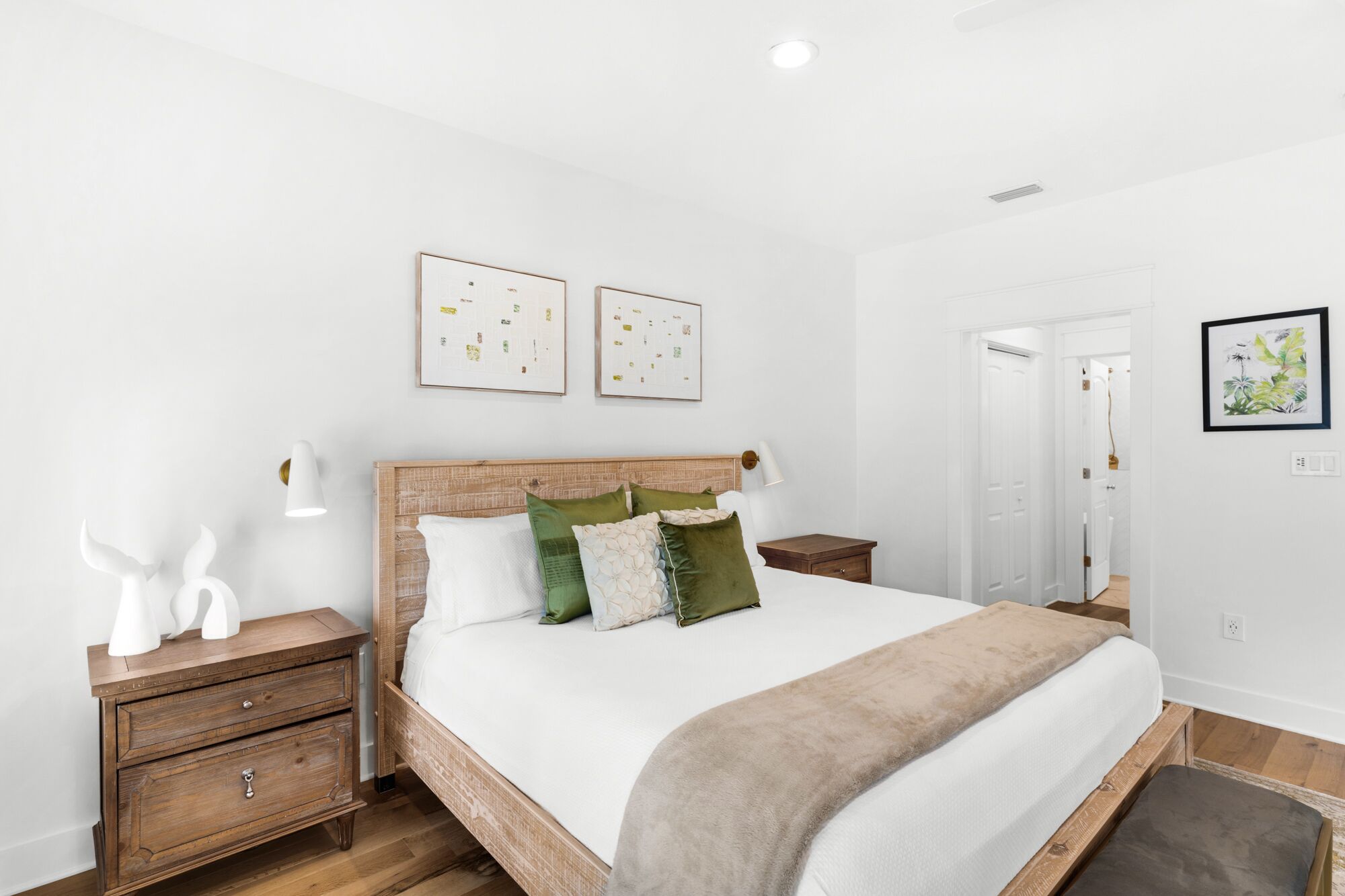 Una camera da letto con un letto a struttura in legno, biancheria da letto bianca e due opere d'arte appese al muro.
