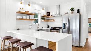 A modern kitchen with a central island, stainless steel appliances, and wooden bar stools. - Private Beach! Gulf Views! Heated Pool! (Seacrest)