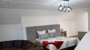 A bedroom with a tufted headboard, a bed with floral bedding, a red throw, a wooden nightstand, a kettle, and a hanging light fixture. - Ojong's Guesthouse (Cape Town)