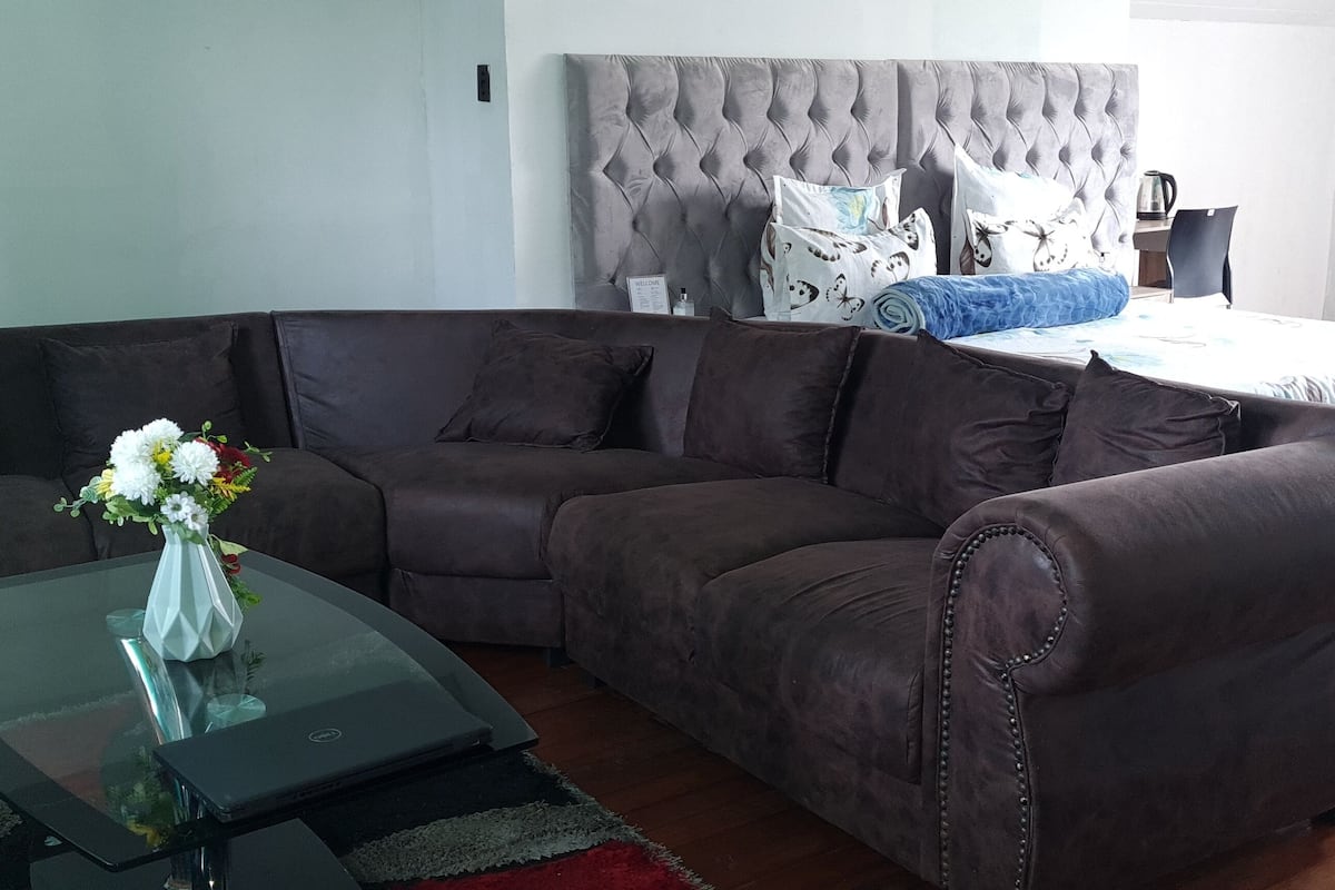 Een moderne woonkamer met een donkerbruine modulaire bank, een glazen salontafel en een bed met een gestuikt hoofdeinde.