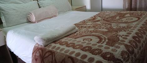 A neatly made bed with a patterned bedspread and pillows, a bedside table, and a wardrobe.