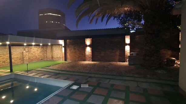 A backyard with a swimming pool, brick walls, and a palm tree. - Ojong's Guesthouse (Cape Town)