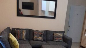 A living room with a sectional sofa, a flat-screen TV mounted on the wall, and a marble floor.