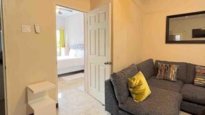 A living room with a grey sofa, a small white table, and a door leading to another room.