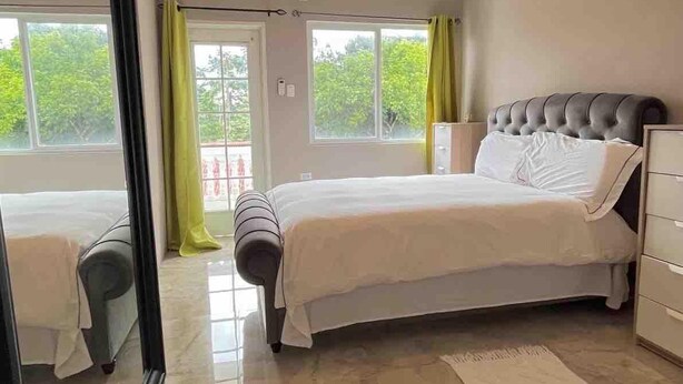 A bedroom with a bed, a ceiling fan, a window, and a view of greenery outside.