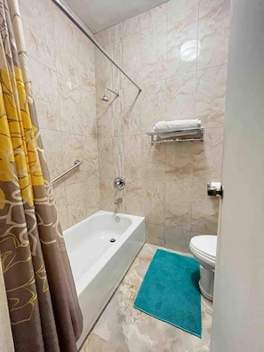A bathroom with a bathtub, toilet, shower, and a towel rack.