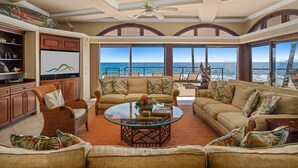 A spacious living room with a large glass table, comfortable seating, and a view of the ocean.