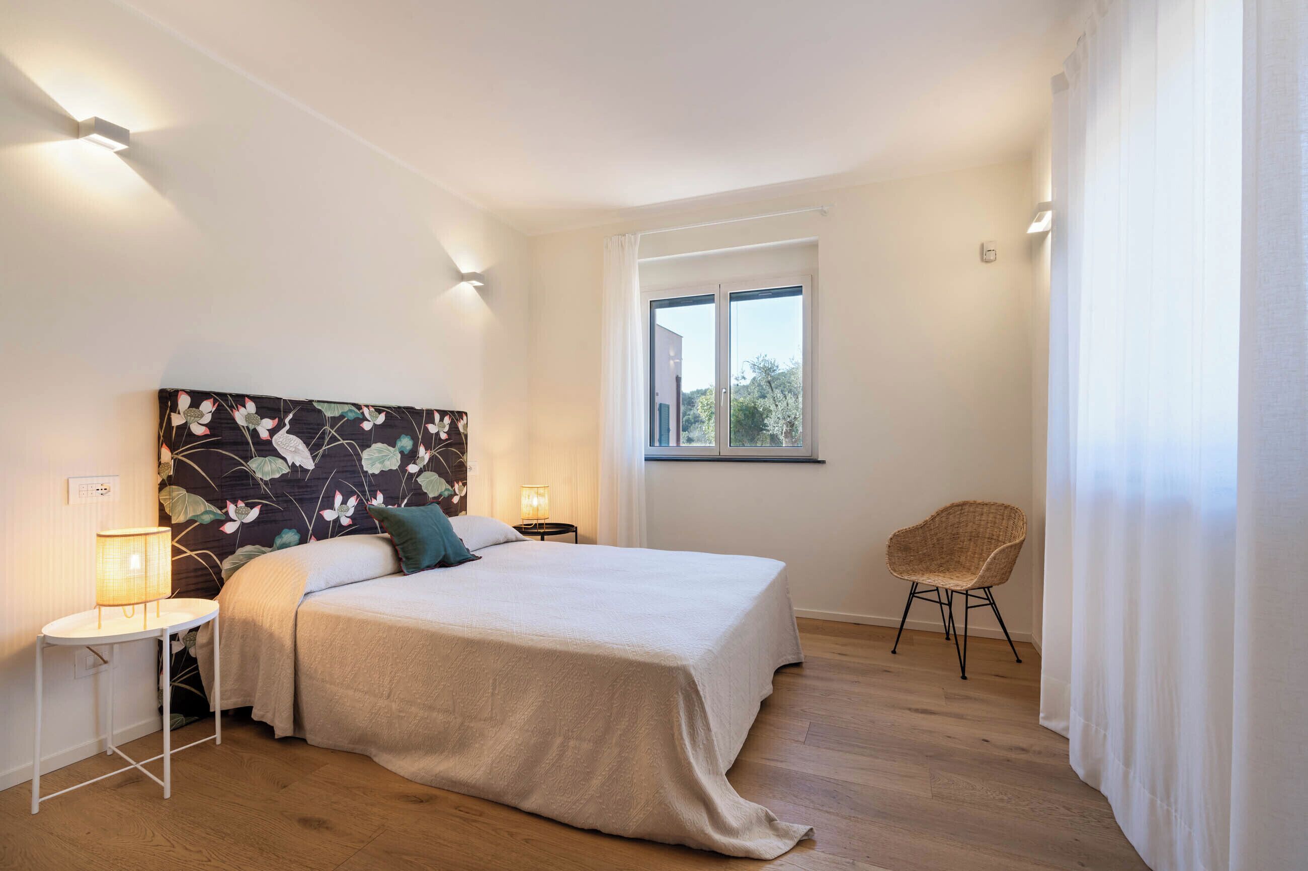 Une chambre à coucher avec un grand lit, des lampes de chevet, une petite table, une chaise et une fenêtre avec des rideaux.