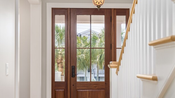 Une porte à deux battants en bois, avec des panneaux de verre, un luminaire au-dessus, et un escalier blanc avec des rampes en bois.