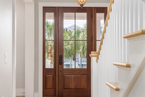 A wooden double door with glass panels, a light fixture above, and a white staircase with wooden handrails. - 521 Carolina Blvd ~ new construction completed March 2024 (Isle Of Palms)