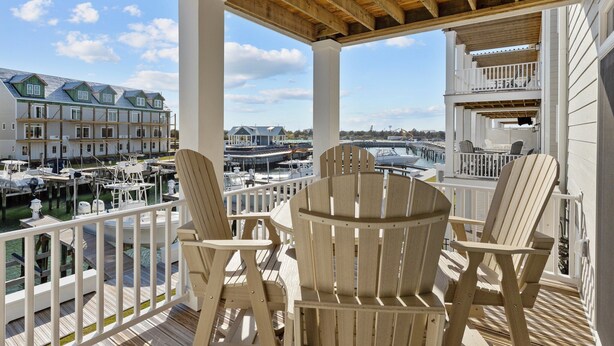 Una terraza techada con sillas de madera y vista a un puerto deportivo con barcos y casas.