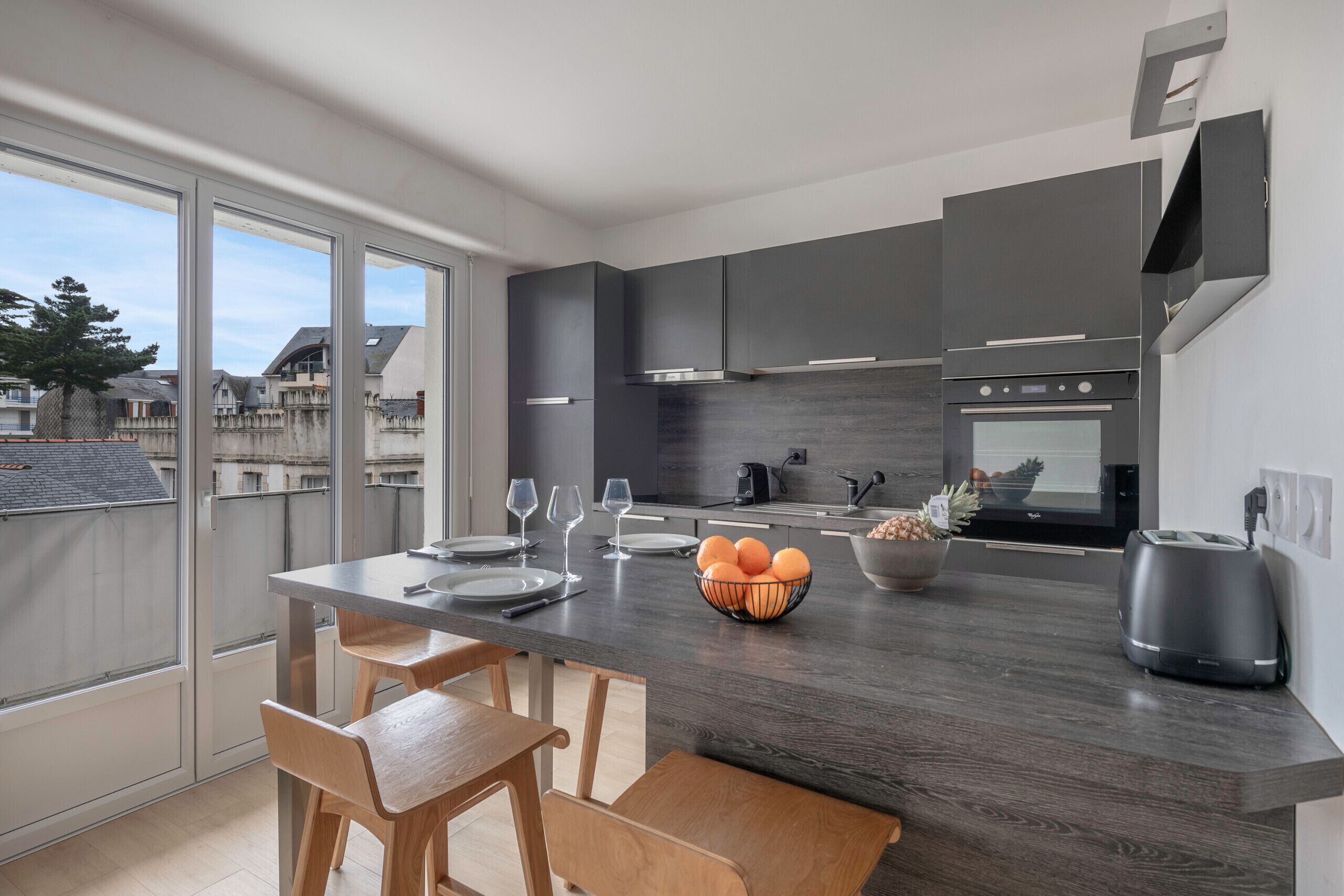 Una cocina moderna con gabinetes oscuros, una isla central con asientos, un ventanal y vistas al vecindario.