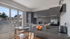 Une cuisine moderne avec des meubles de couleur sombre, un îlot central doté de sièges, une grande fenêtre et une vue sur le quartier.