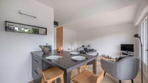 Un espace repas moderne avec une table en bois foncé mise pour deux personnes, des chaises en bois, un canapé gris et un téléviseur en arrière-plan.