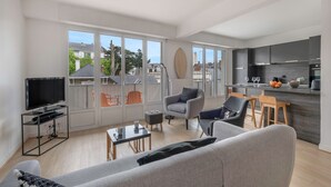 Un salon moderne comprenant un canapé, des fauteuils, un téléviseur et un coin repas avec des chaises et une table.
