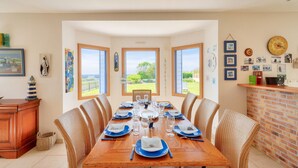 A dining area with a wooden table set for six, surrounded by wicker chairs, with a brick wall and a view of the outdoors. - Sea view, 200m from the beach, house for 9 (Plovan)