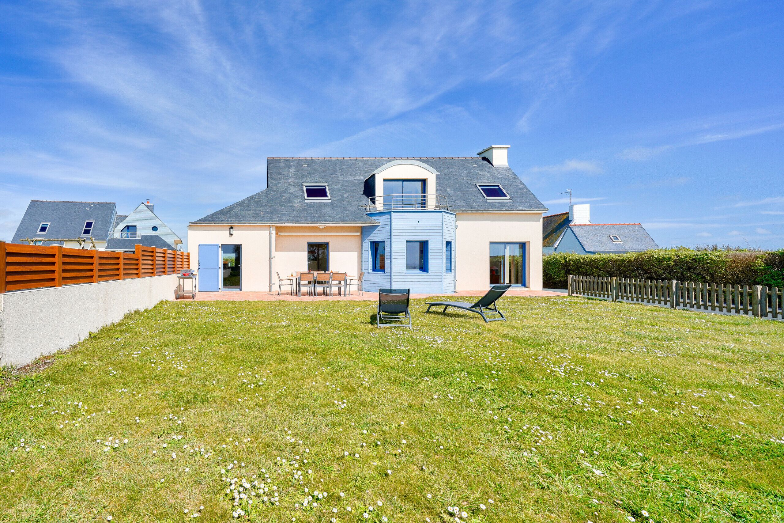 A two-story house with a large backyard, a wooden fence, and a clear sky.