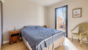 A bedroom with a bed, a nightstand, a chair, and a large window. - Saint-Vincent-sur-Jard, house for 5 (Saint-Vincent-sur-Jard)