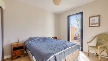 Une chambre à coucher avec un lit, une table de chevet, une chaise et une grande fenêtre.