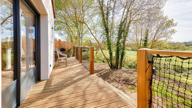 A wooden deck with a glass door leading to a room, surrounded by trees and a view of a field. - Saint-Vincent-sur-Jard, house for 5 (Saint-Vincent-sur-Jard)