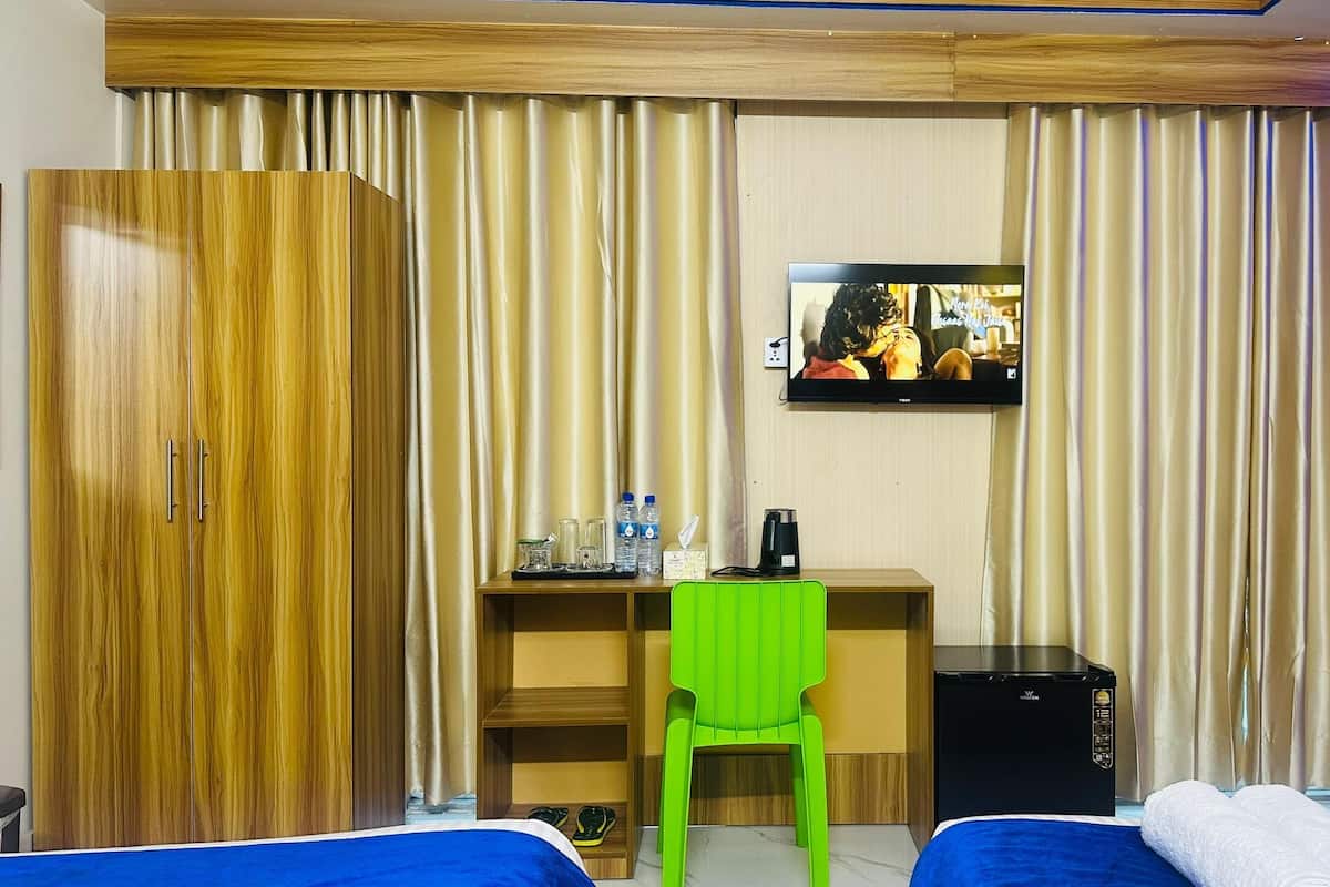 A hotel room with a wooden wardrobe, a desk with a chair, a TV, and a bed.