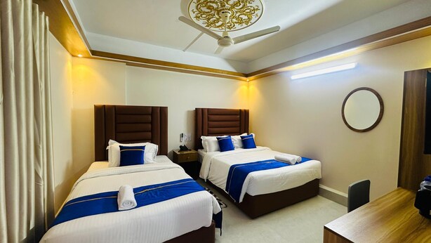 Een hotelkamer met twee bedden, elk met een blauw-witte spreideken, een houten hoofdeinde en een nachtkastje met een lamp.