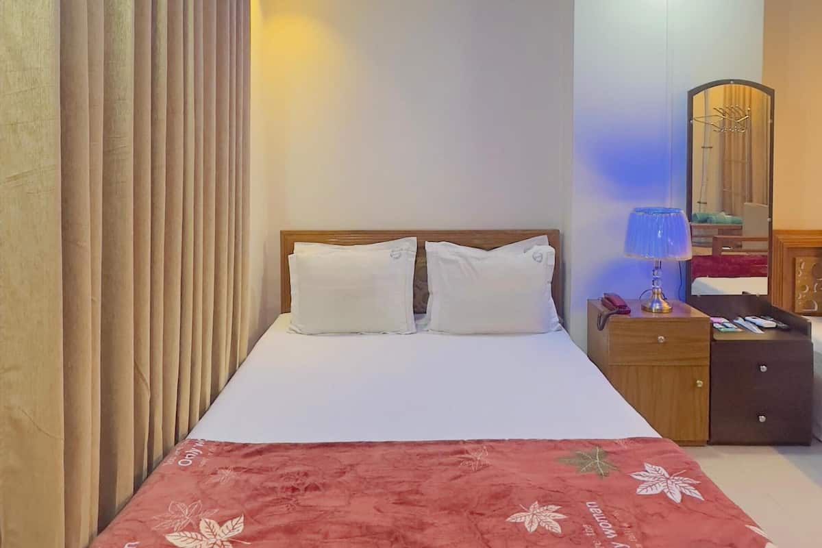A hotel room with a bed, a nightstand, a lamp, a mirror, and a ceiling with a decorative design.