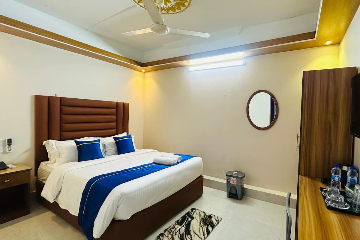 A hotel room with a large bed, a bedside table, a TV, a mirror, and a small trash bin.