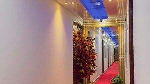 Een hotelgang met een rode loopbaan, houten plantenbakken met planten en een blauw verlicht plafond.