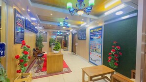 Een hotel lobby met een receptiebalie, een zithoek en een groene wand met een poster.