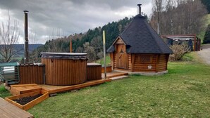Een houten blokhut met schuin dak, een jacuzzi en een klein terras.
