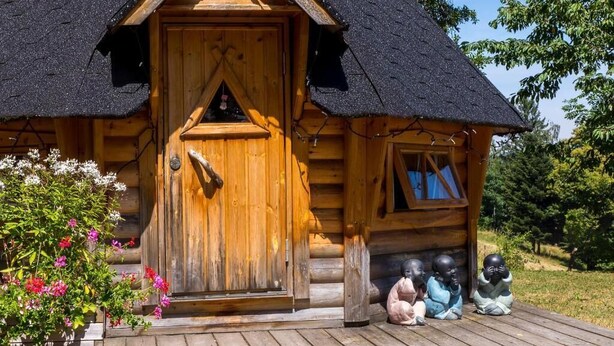 Een houten blokhut met rieten dak, een houten deur en een klein raam.