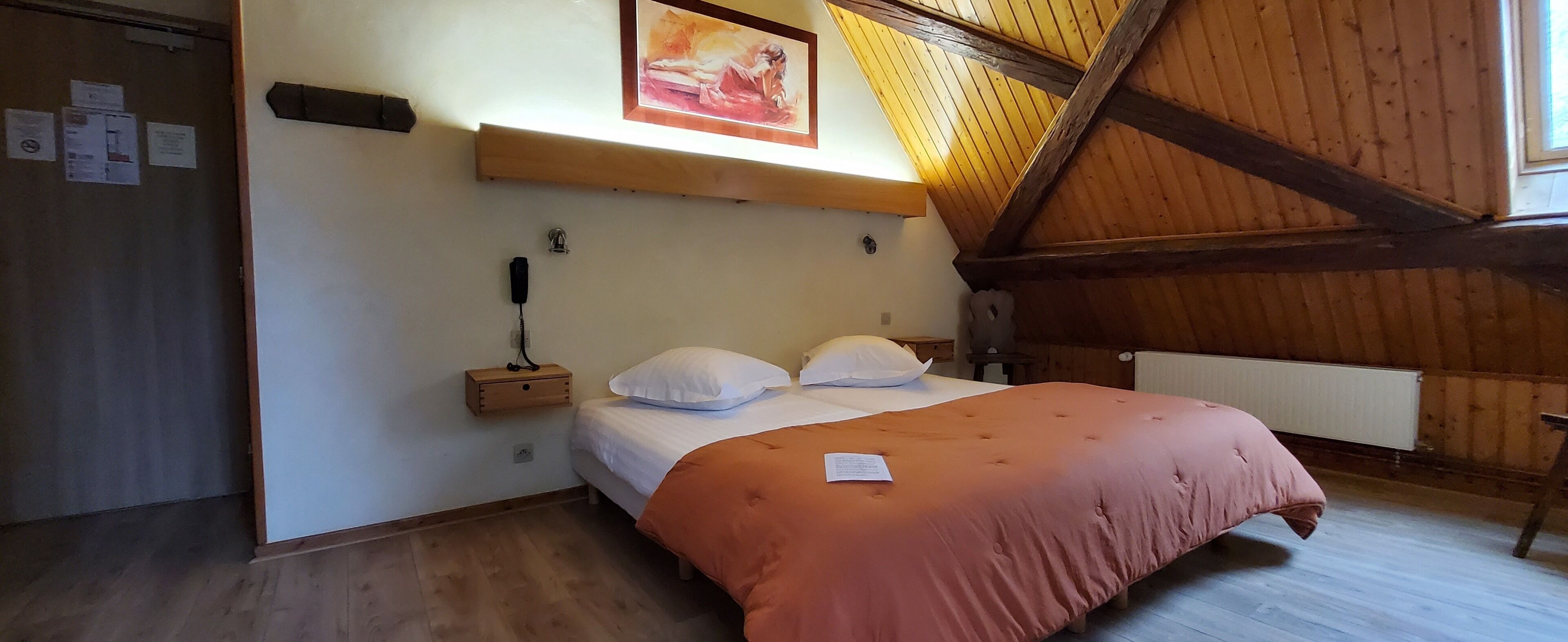 Un dormitorio con techo de madera, una cama con almohadas blancas, una mesita de noche de madera y un cuadro sobre la cama.