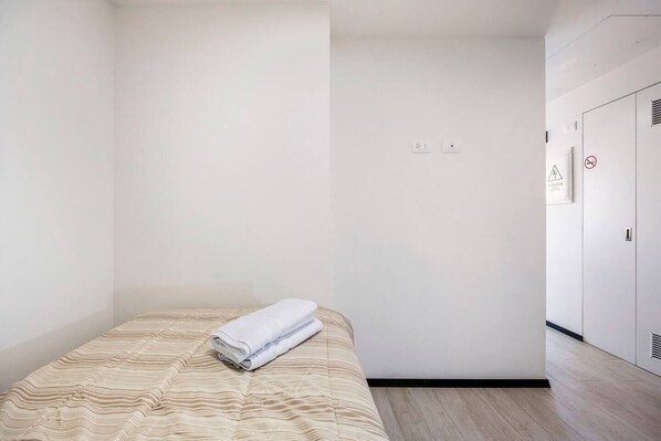 A minimalist bedroom with a bed, a folded towel, and a wardrobe.