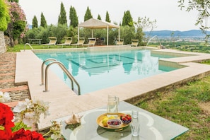 A pool with lounge chairs and a table with a pitcher of water and fruit.