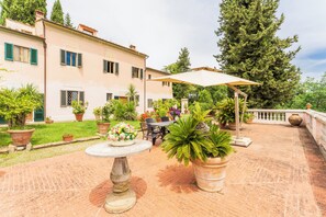 A courtyard with a table and chairs, surrounded by potted plants and a large tree.