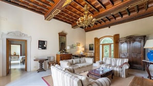 Ein geräumiges Wohnzimmer mit hoher Decke, Holzbalken und einer Chandelier. Zwei Sofas und ein Couchtisch sind vorhanden.