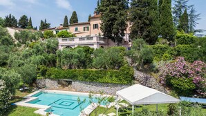 A swimming pool with a white canopy, surrounded by lush greenery and a stone wall.