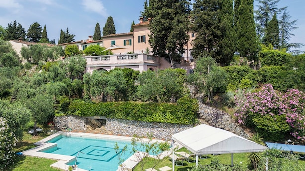 Ein Swimmingpool unter einer weißen Markise, umgeben von üppiger Vegetation und einer Steinmauer.
