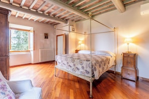 A bedroom with a four-poster bed, wooden flooring, a radiator, a window, and a nightstand with a lamp.