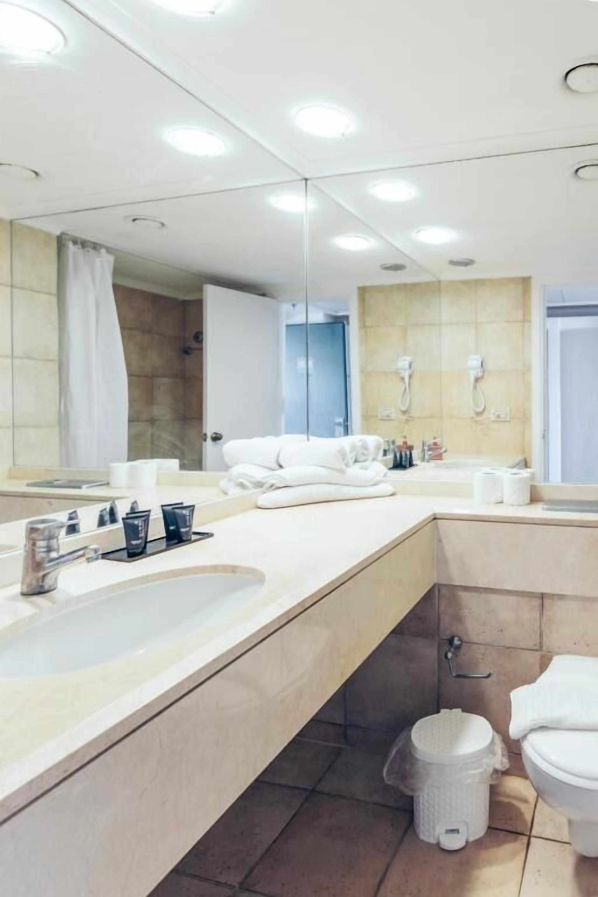 Un baño moderno con un espejo grande, un lavamanos con tocador, un inodoro y una zona de ducha.
