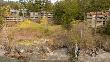 A coastal hotel with multiple balconies, a rocky shoreline, and a forested backdrop.
