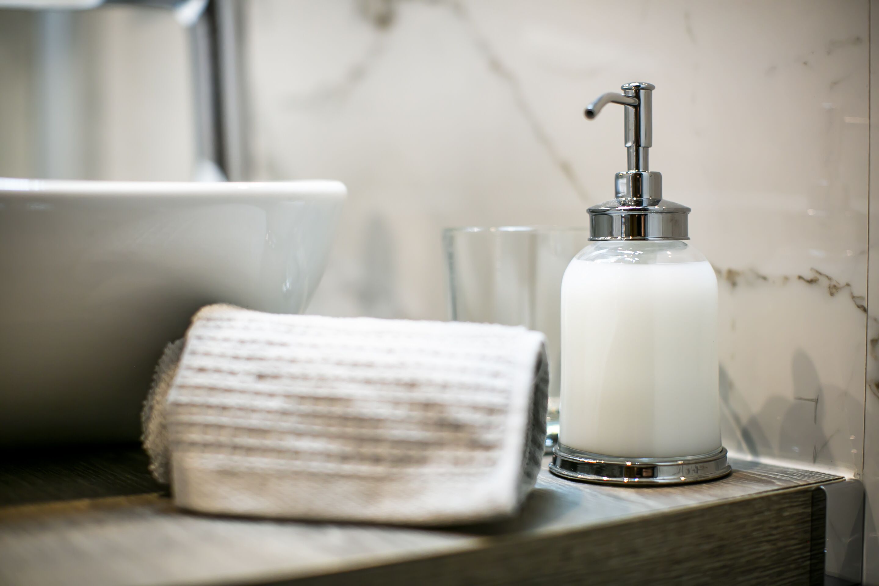 A bathroom with a white sink, a glass of water, and a soap dispenser on a wooden surface.
