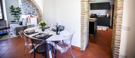 A dining area with a round table, clear chairs, and a brick archway leading to a kitchen.