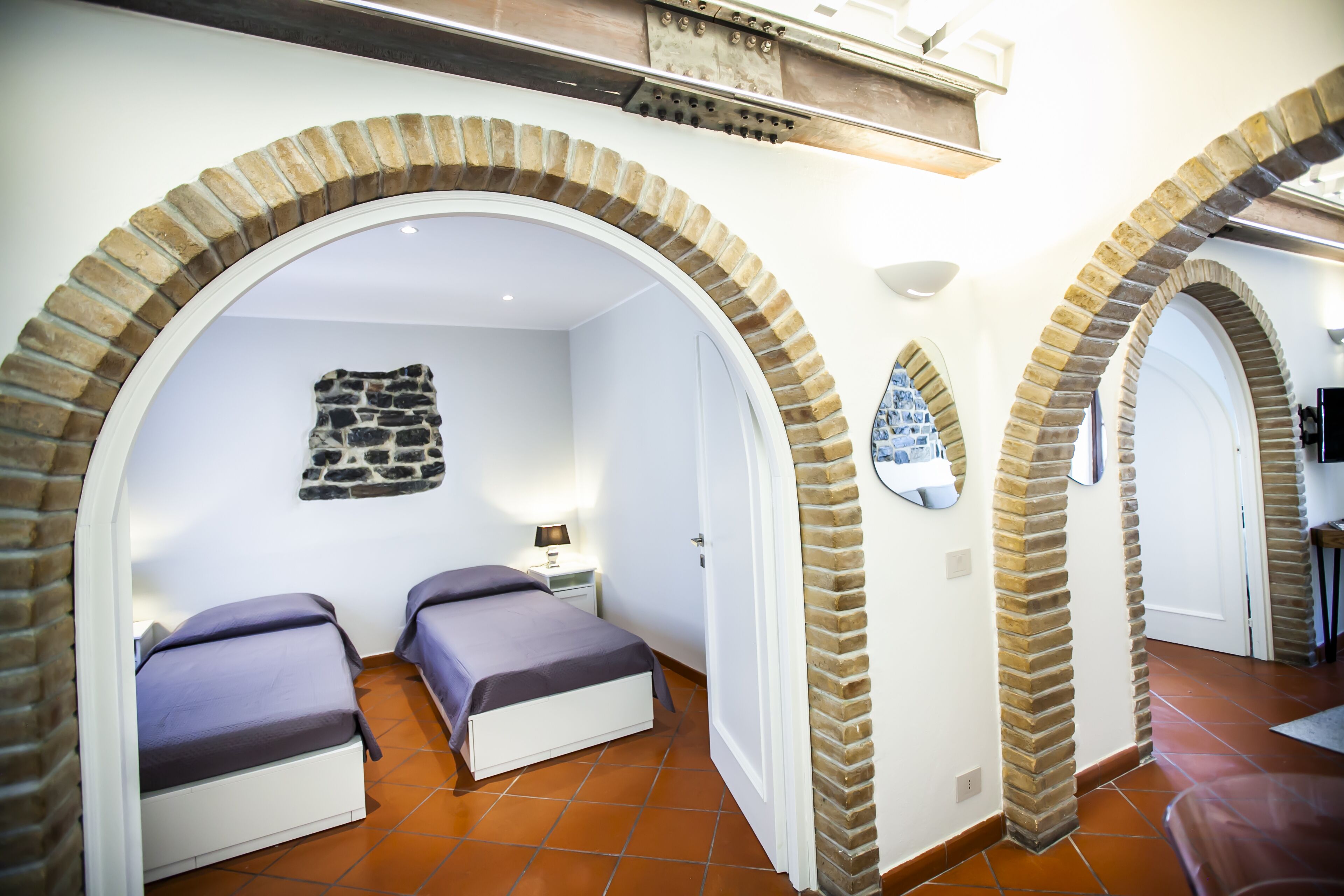 A room with two beds, a stone wall, and brick arches.