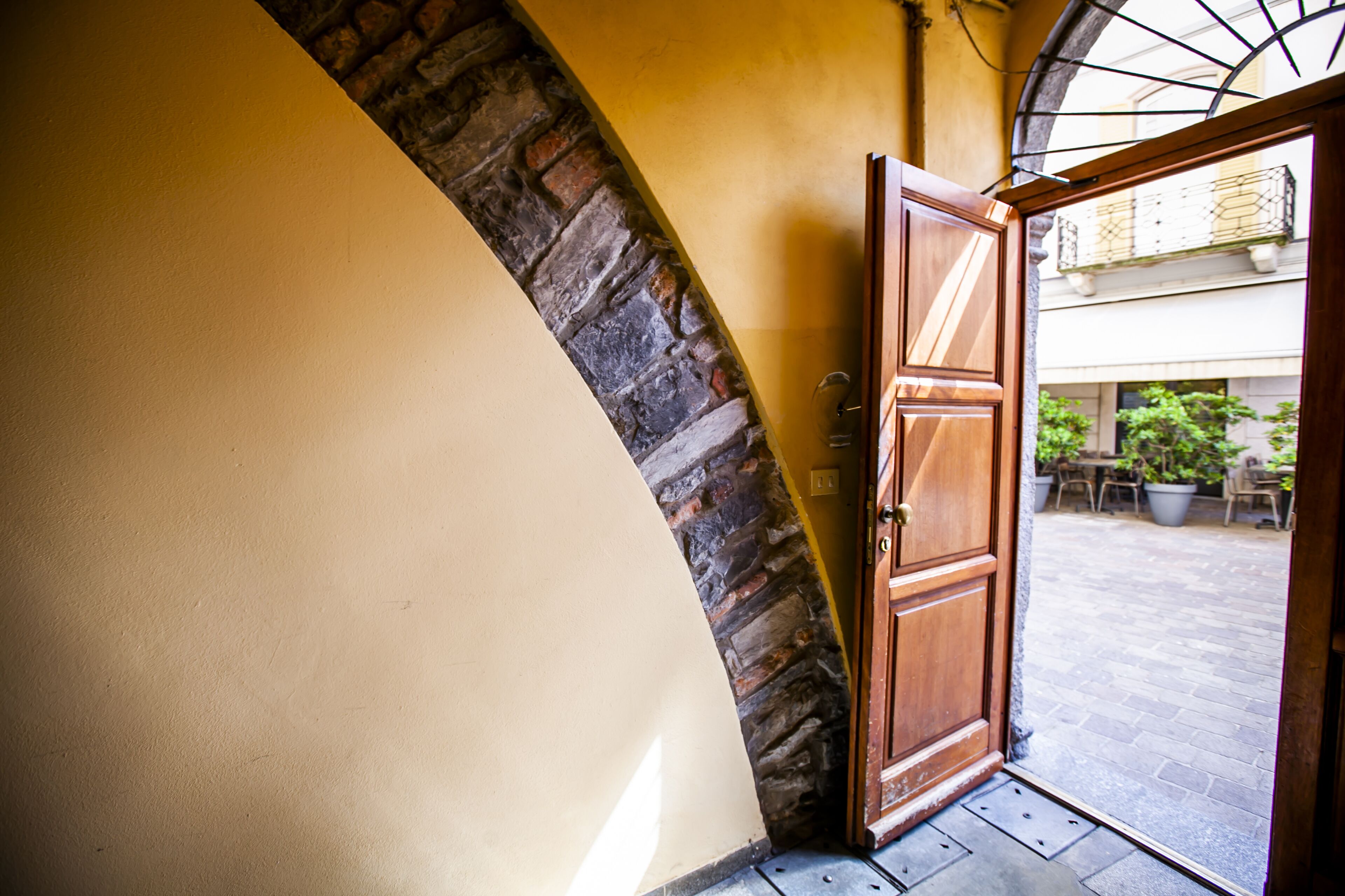 Entrada de hotel com arco de pedra, porta de madeira e vista para o pátio com área de estar ao ar livre.