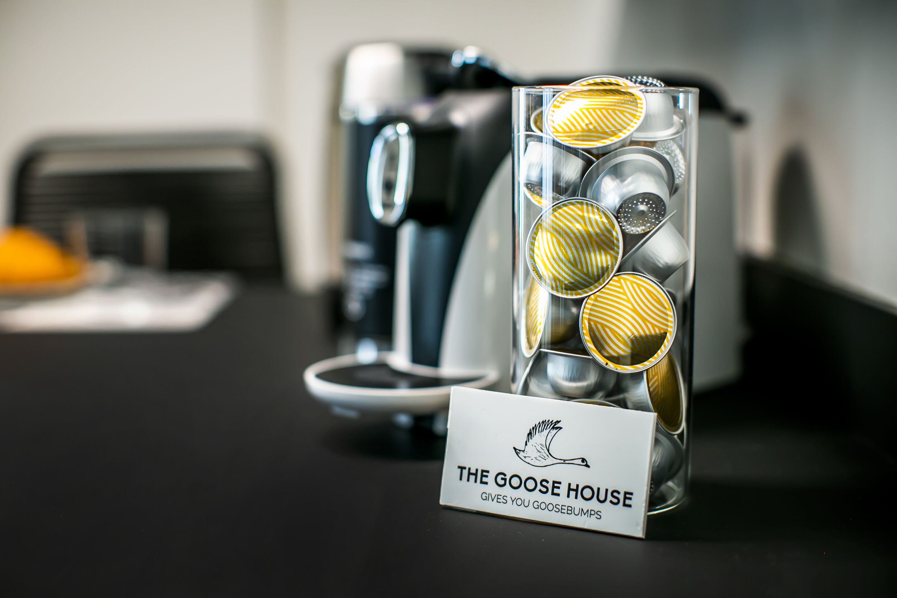 Eine Kaffeemaschine und ein Glasbehälter mit dem Aufdruck 'The Goose House' auf einem Tisch.