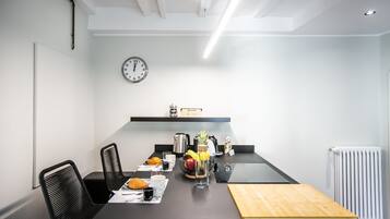 Ett modernt kök med en svart bänkskiva, vita väggar och en klocka. Det finns stolar, ett bord med mat på och ett element.