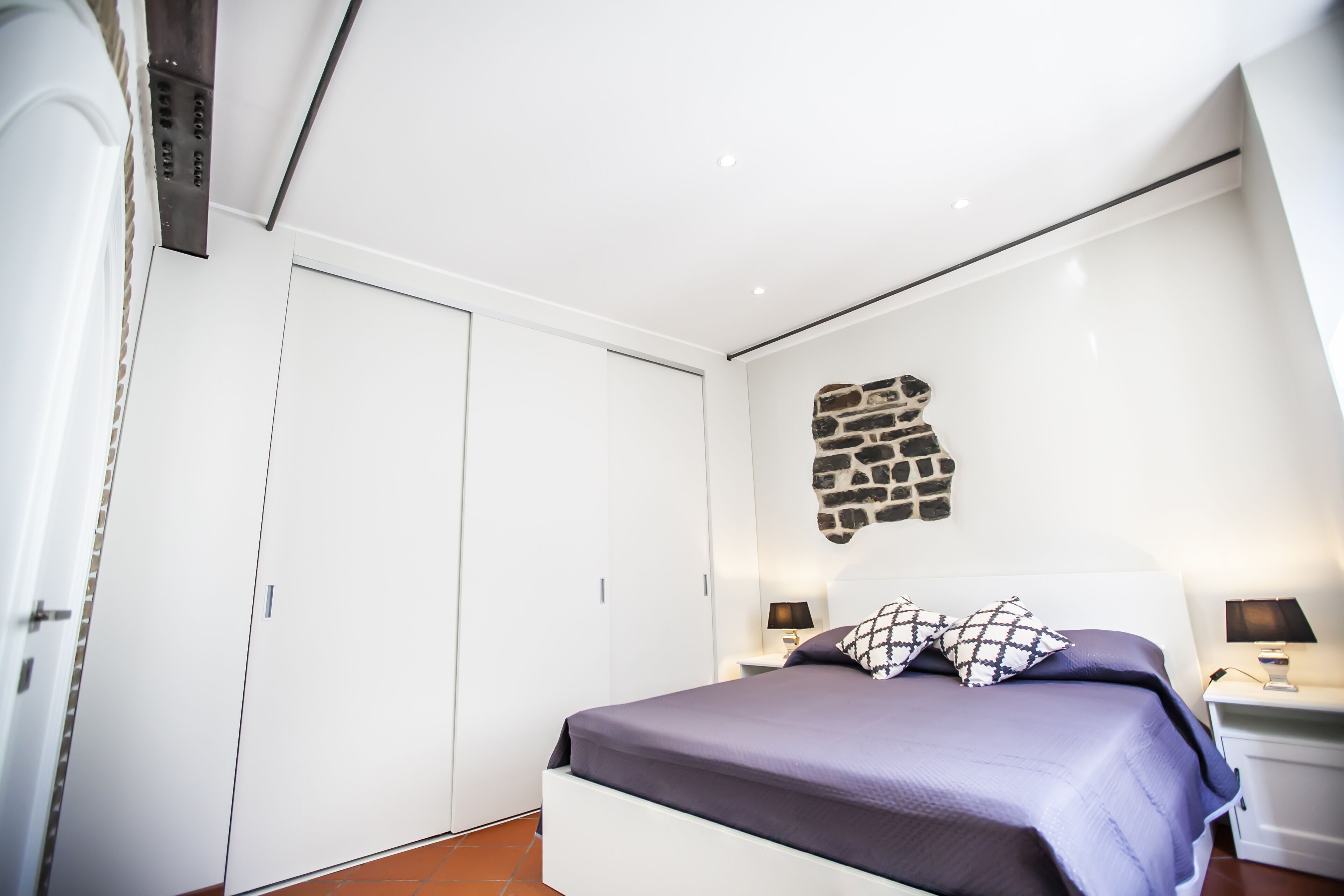 A bedroom with a bed, nightstands, a wardrobe, and a stone wall decoration.